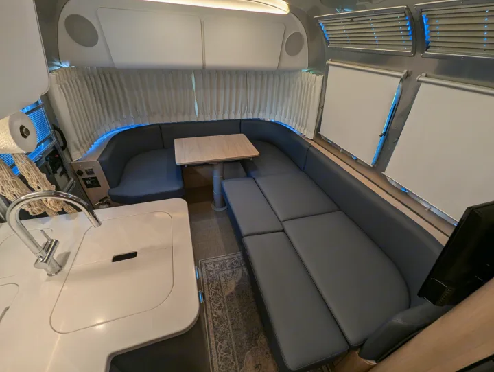 Step inside this sleek RV rental! Features a modern kitchen, spacious dinette, and cozy seating area with blue accents.. Airstream Globetrotter 2024