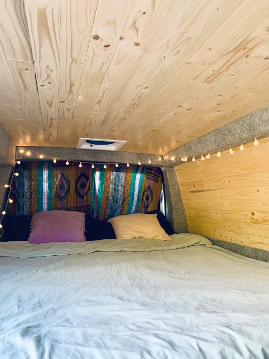 Cozy RV rental interior with wooden ceiling, string lights, and a colorful blanket over a comfy bed.. Gmc Savanna 2016