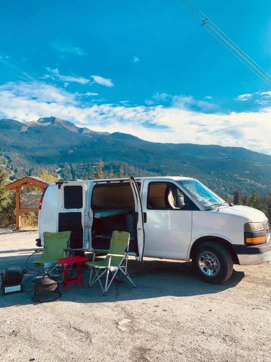 Scenic RV rental setup: white campervan, chairs, grill, fire pit by mountains. Perfect outdoor living!. Gmc Savanna 2016