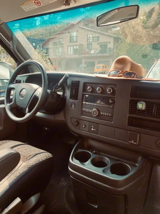 Inside a GMC van, possibly an RV rental, showing the dashboard with a hat and sunglasses. Ready for the open road.. Gmc Savanna 2016