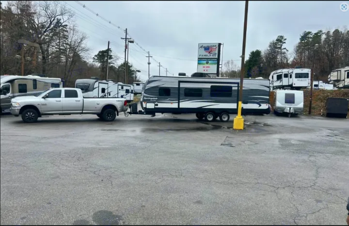 A truck tows a large travel trailer at an RV lot. Many RVs are available for rental or sale, ready for adventure.. Keystone Springdale 2016