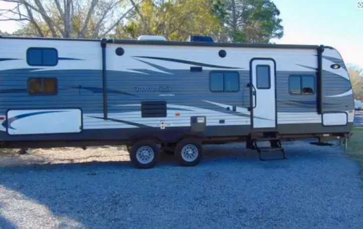 This spacious grey & white travel trailer RV rental, with multiple windows & a side door, is parked on a gravel lot.. Keystone Springdale 2016