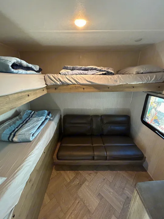 RV rental interior featuring two bunk beds with bedding, a comfortable sofa, and herringbone flooring, bathed in warm light.. Palomino Puma 2022