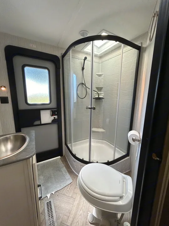 This RV rental bathroom features a compact corner shower, toilet, sink, and an exit door, ideal for travel.. Palomino Puma 2022