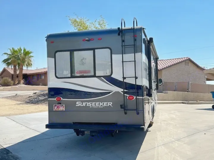 Rear view of a grey and white Sunseeker RV rental, a recreational vehicle parked on pavement under a sunny sky.. Forest River Sunseeker 2018