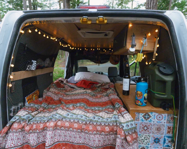 Cozy RV rental interior: a comfortable bed with a patterned blanket, warm string lights, and practical storage solutions.. Ford Transit 2011