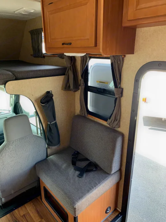 RV rental interior: a clean view of the cab-over bunk, a seat with a seatbelt, window with curtains, and wood cabinets.. Thor Majestic 2015