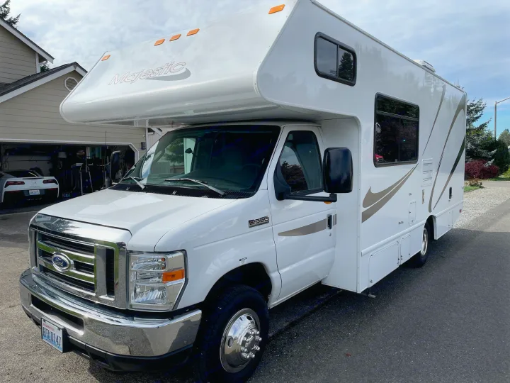 Spotless white Majestic Class C RV rental on a Ford E-350 chassis, parked on asphalt. Awaiting its next road trip.. Thor Majestic 2015