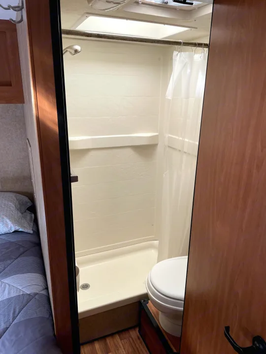 RV rental: A compact bathroom featuring a shower with curtain, and a toilet, seen from the doorway with a bed nearby.. Thor Majestic 2015
