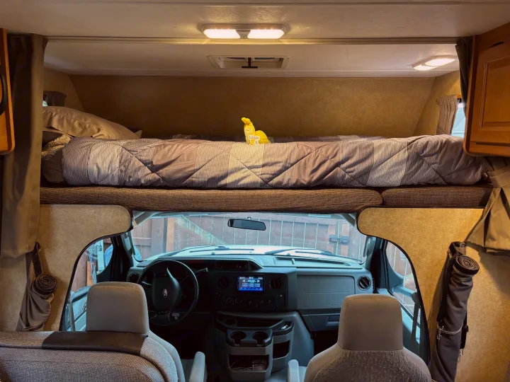 Inside an RV rental: View from the living area showing the front cockpit and an overhead cab-over bed with bedding.. Thor Majestic 2015