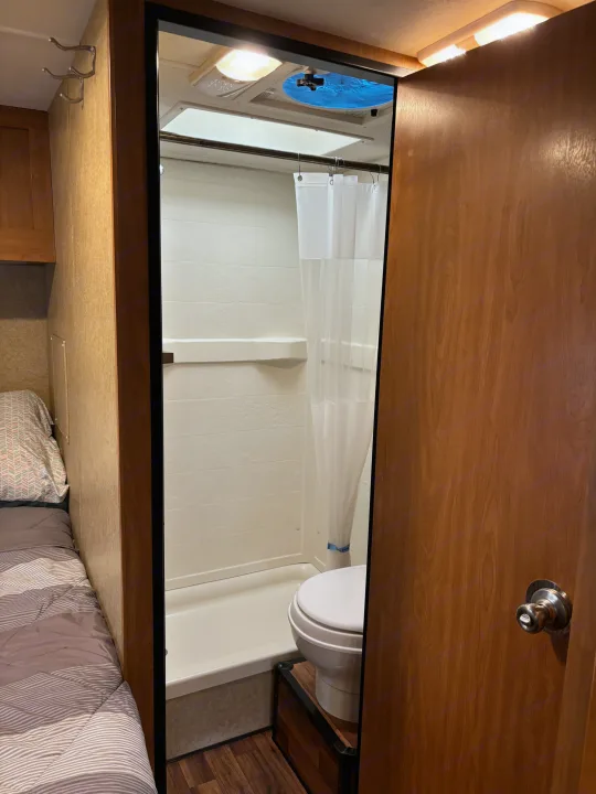 View of an RV rental's compact interior, showing a bed area on the left and a bathroom with a shower, toilet, and vent.. Thor Majestic 2015