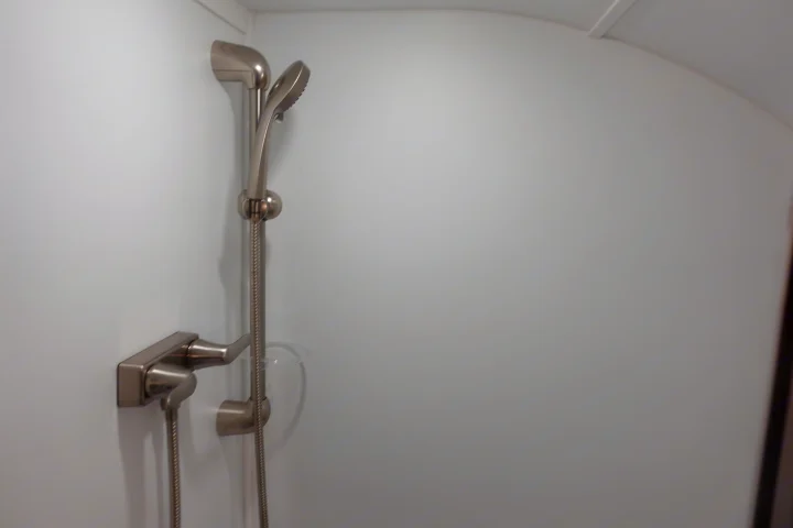 RV rental shower: Modern brushed nickel faucet, handheld showerhead, and small clear holder on white wall.. Little Guy Mini-Max 2024