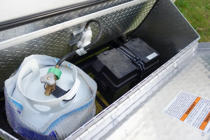 RV rental equipment: An open aluminum storage box with a propane tank, battery, and visible safety warnings.. Little Guy Mini-Max 2024