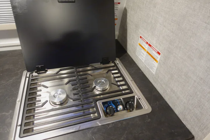 Dometic two-burner propane cooktop in an RV rental. The stainless steel stove has its black cover open, revealing control knobs.. Little Guy Mini-Max 2024