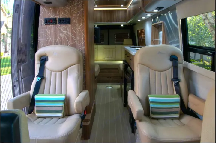Interior of a luxurious RV rental featuring two tan leather captain's chairs, an aisle leading to a compact kitchen & living area.. Airstream Interstate 2017