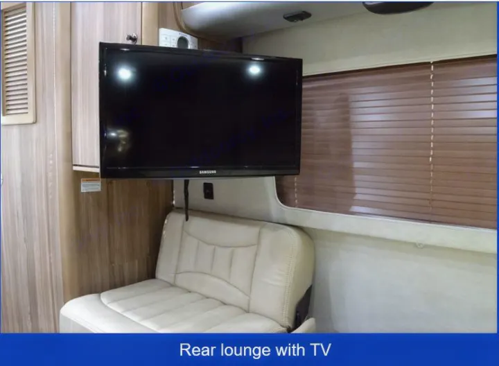 Cozy RV rental interior with a mounted TV above a cream lounge seat, wood paneling, and brown window blinds.. Airstream Interstate 2017