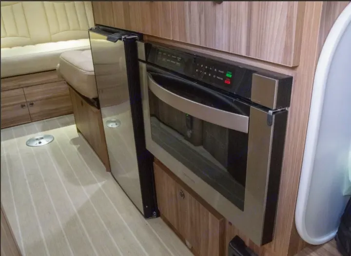 RV rental's compact kitchen: built-in stainless steel microwave/oven, refrigerator, and bench seating on wood-look floor.. Airstream Interstate 2017