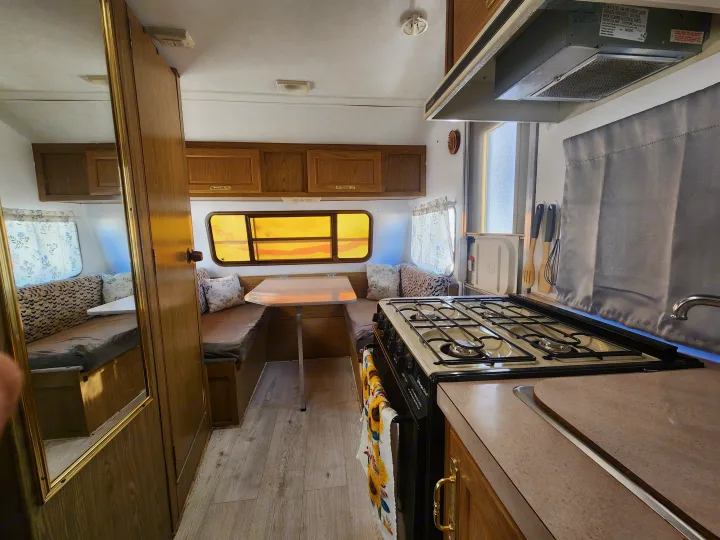 RV rental interior features a compact kitchen with stove, dining table, and cozy bench seating that converts to a bed.. Fleetwood Wilderness 1991