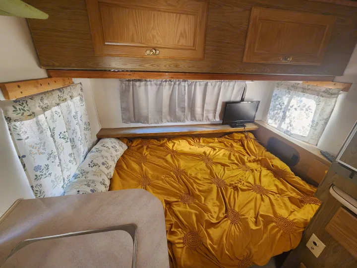 Inside an RV rental: a cozy bedroom with a vibrant yellow bed, floral curtains, and TV for a comfortable stay.. Fleetwood Wilderness 1991