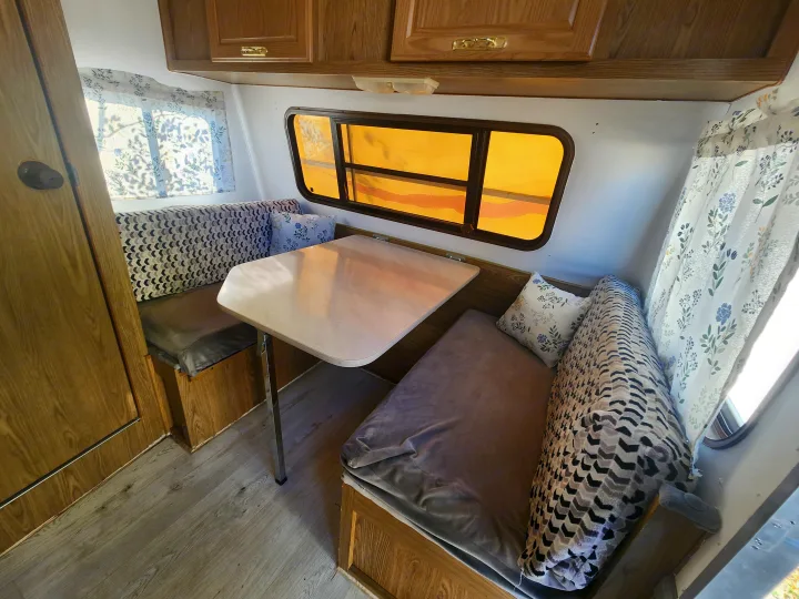 Cozy RV rental dinette area with table, patterned cushions, and warm lighting. Perfect for road trip meals.. Fleetwood Wilderness 1991