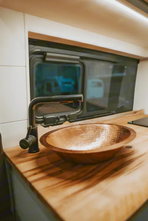 RV rental's inviting kitchen: hammered copper sink, sleek black faucet, and beautiful wood counter.. Noke Van Co. Rory 2021