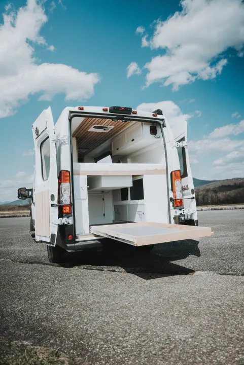 Explore our custom-built RV rental camper van with open rear doors, showing its wood interior and convenient pull-out storage.. Noke Van Co. Rory 2021