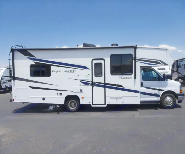 White Class C RV rental with bold dark blue and black graphics, parked on asphalt under a clear blue sky. Ideal for road trips.. Coachmen Freelander 2023
