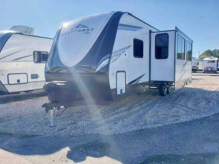 Bright white travel trailer (RV) on gravel lot, perfect for RV rental. Slide-out open on sunny day.. East to West Alta 2024