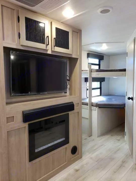 RV rental interior: Living area with TV, fireplace, and bunk beds, all in light wood tones.. East to West Alta 2024
