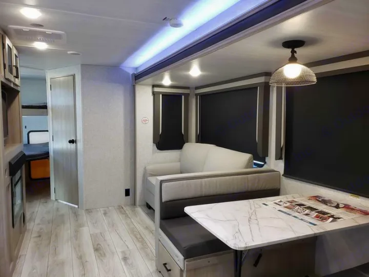 Spacious modern RV rental interior featuring a living/dining area, bunk beds visible, and wood-look flooring.. East to West Alta 2024