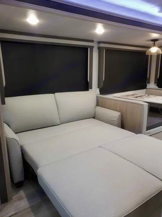 Cozy RV rental interior with a light-colored sofa converting into a bed, alongside blackout shades and a dining area.. East to West Alta 2024