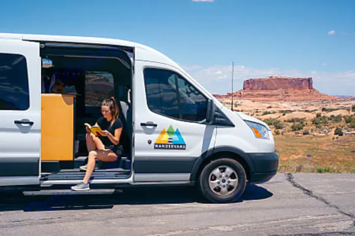 Find your escape with an RV rental. A woman reads inside a WANDERVANS campervan, parked overlooking vast red rock landscapes.. Ford transit 2017