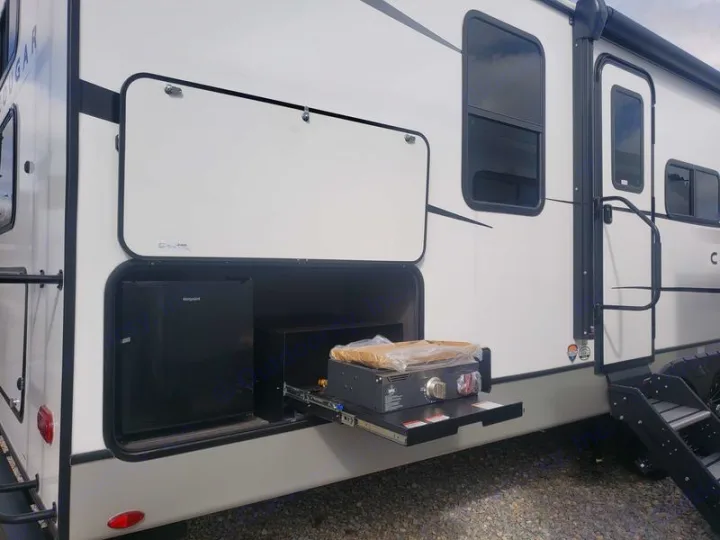 This RV rental boasts an outdoor kitchen with a mini-fridge and a pull-out stove in an open side compartment.. Keystone RV Cougar 2024