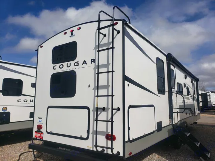 Rear and side view of a white Cougar Keystone RV travel trailer with a ladder and awning, suitable for rv rental.. Keystone RV Cougar 2024