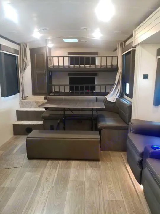 Inside a modern rv rental: bunk beds, dining booth, plush seating, and light wood-look flooring. Brightly lit interior.. Keystone RV Cougar 2024