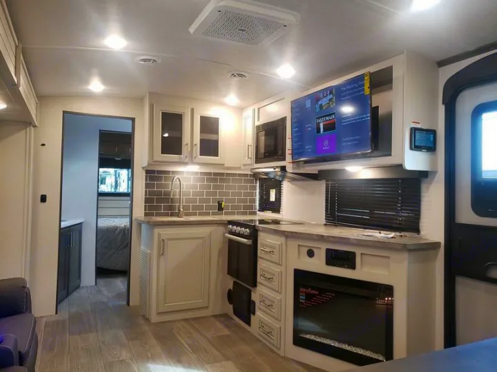Modern RV rental interior: full kitchen, living area with TV & fireplace, and a bedroom beyond.. Keystone RV Cougar 2024