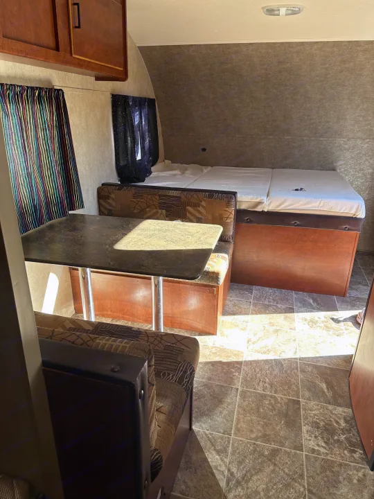 Cozy RV rental interior shows a dinette table, patterned booth seats, and a bed. Light streams onto the tiled floor.. Forest River Salem Cruise Lite 2017