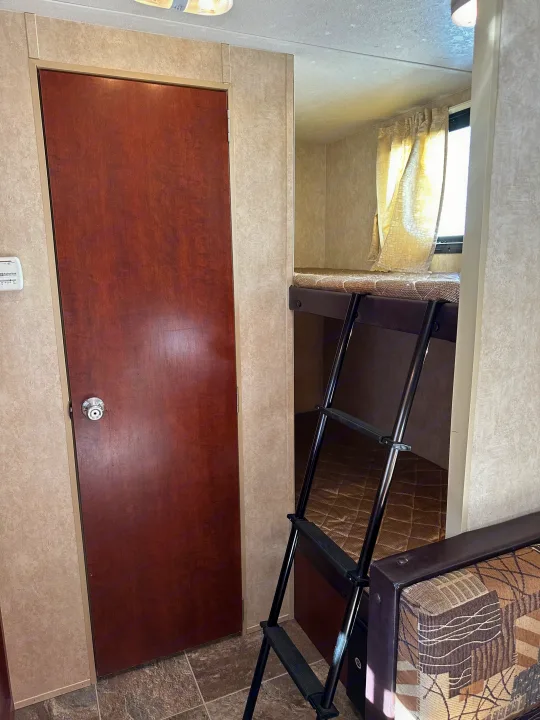 RV rental interior shows a wooden door, thermostat, and bunk beds with a ladder, indicating a cozy, functional space.. Forest River Salem Cruise Lite 2017