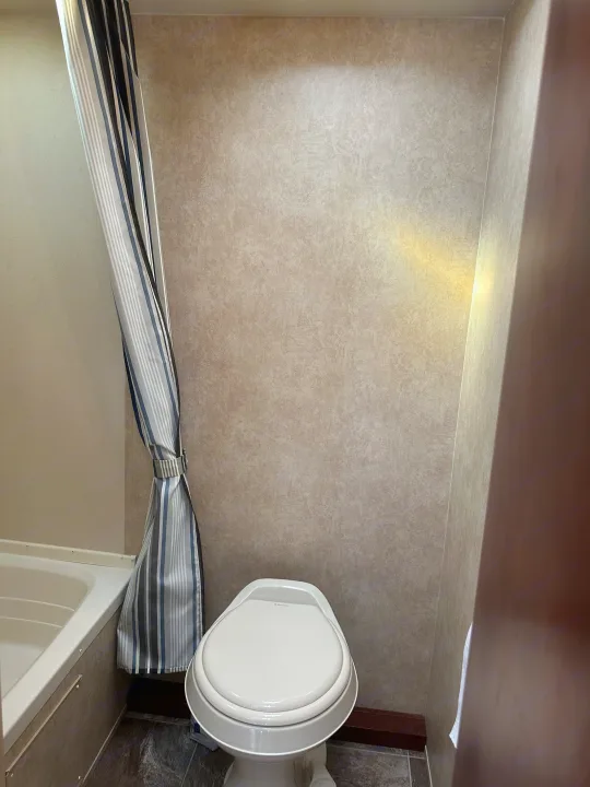 RV rental's compact bathroom: white toilet, bathtub, and tied striped shower curtain.. Forest River Salem Cruise Lite 2017