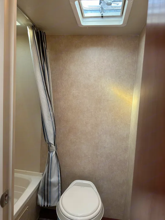 RV rental bathroom featuring a white toilet, tub/shower with a striped curtain, and overhead vent.. Forest River Salem Cruise Lite 2017