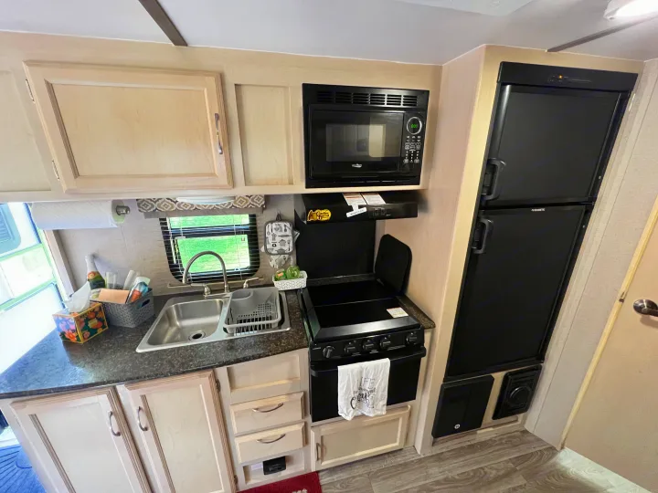 RV rental kitchen with practical amenities: light wood cabinets, black microwave, stove, double sink, and Dometic fridge.. Winnebago Micro Minnie 2306BHS 2019