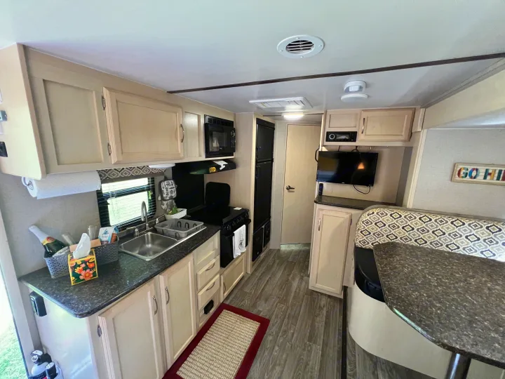 Modern RV rental kitchen & dinette, with light cabinets, dark counters, sink, stove, microwave, TV, and patterned booth seating.. Winnebago Micro Minnie 2306BHS 2019
