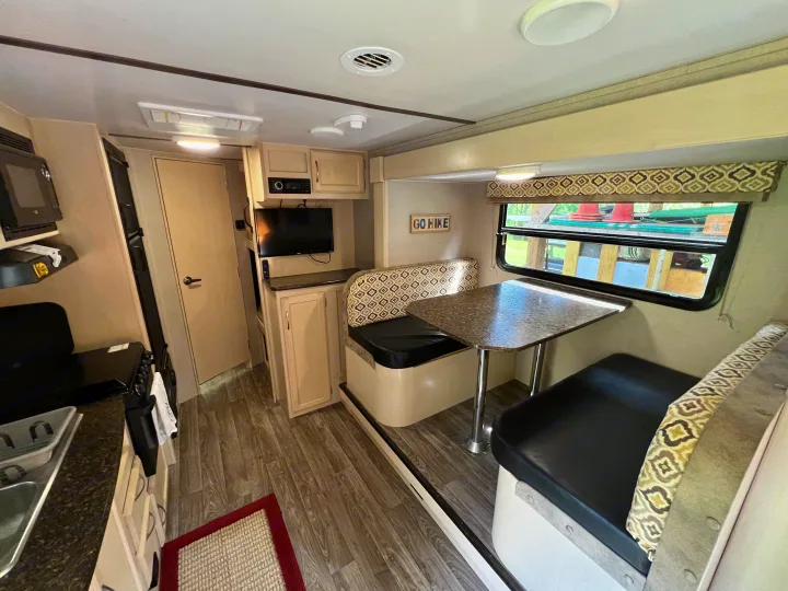 RV rental interior showing a dinette with patterned cushions, a compact kitchen, and a TV.. Winnebago Micro Minnie 2306BHS 2019