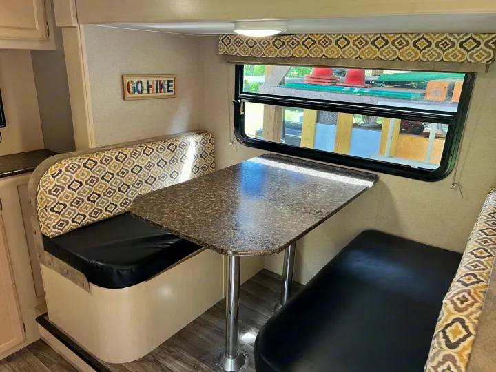 Inside this rv rental, a dinette offers U-shaped bench seating with patterned backs, a granite-look table, and a window overlooking greenery.. Winnebago Micro Minnie 2306BHS 2019