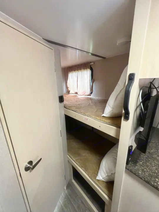 Cozy RV rental interior featuring comfortable bunk beds with a pillow and an adjacent TV area.. Winnebago Micro Minnie 2306BHS 2019