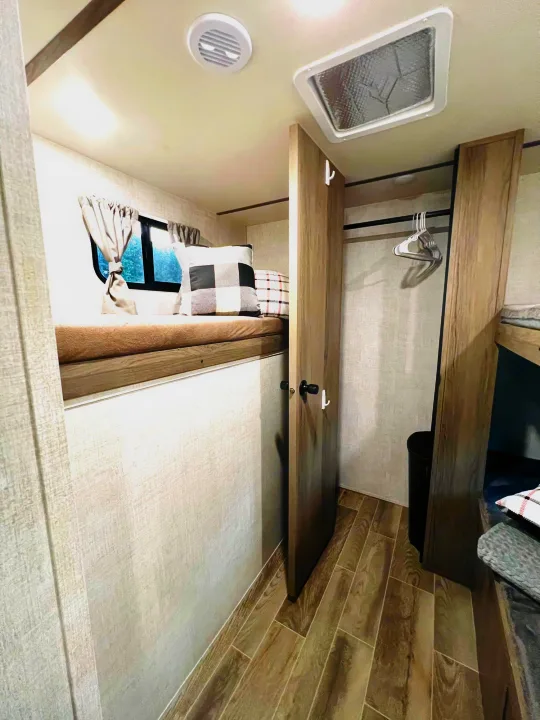 RV rental interior: cozy bunk bed with window, ample wardrobe space with hangers, and stylish wood-look flooring.. Gulf Stream Gulf Stream 2021