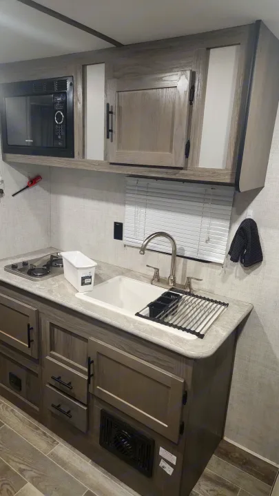 A bright and functional rv rental kitchen featuring a microwave, cooktop, sink with drying rack, and cabinets.. Gulf Stream Ameri-Lite Super Lite 2022