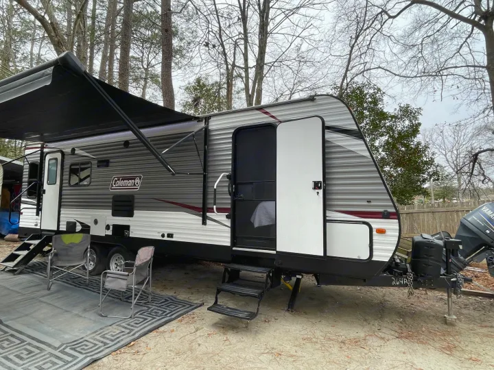 RV rental: A Coleman travel trailer is set up at a sandy campsite with an extended awning, outdoor rug, and chairs.. Coleman Lantern 2019
