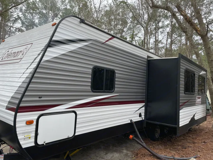 An RV rental at a wooded campsite with its slide-out extended, showing a typical setup for outdoor camping and travel.. Coleman Lantern 2019