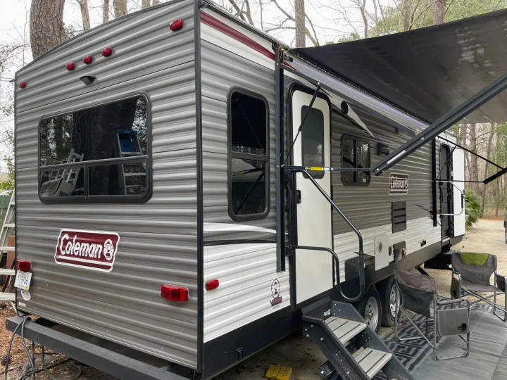 Grey Coleman travel trailer with extended awning, steps, and chairs at a campsite, ready for your next rv rental trip.. Coleman Lantern 2019